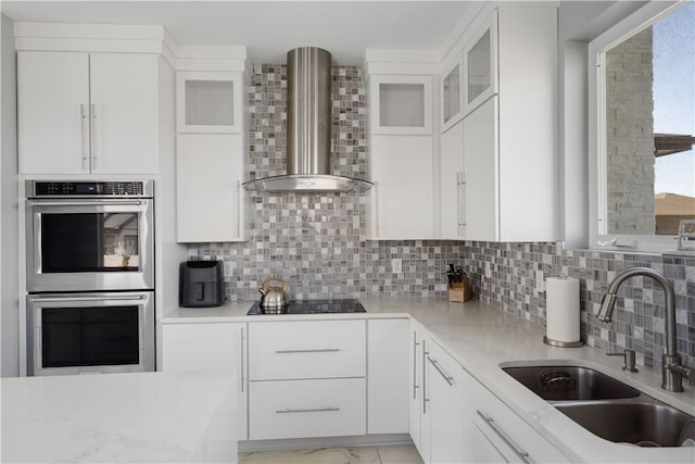 kitchen with a sink, tasteful backsplash, stainless steel double oven, wall chimney exhaust hood, and black electric stovetop