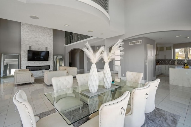 dining area featuring a stone fireplace, a high ceiling, light tile patterned flooring, and visible vents