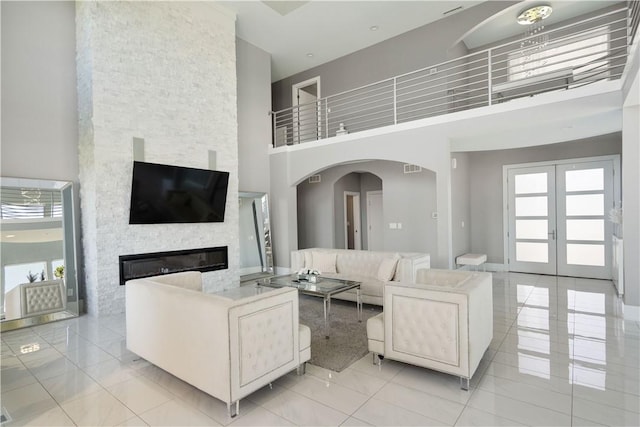 living area featuring visible vents, french doors, arched walkways, a stone fireplace, and a towering ceiling