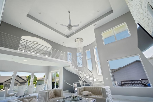 living room featuring stairway, a raised ceiling, ceiling fan, and a towering ceiling