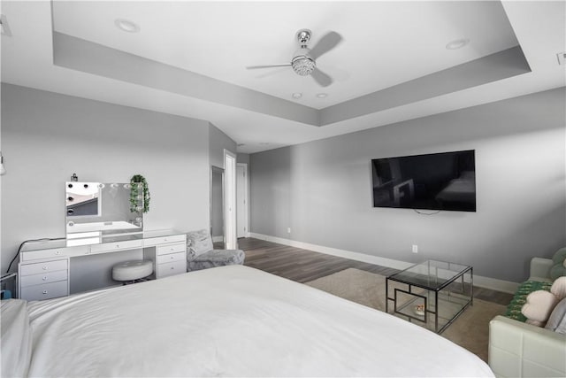 bedroom featuring visible vents, a tray ceiling, wood finished floors, baseboards, and ceiling fan