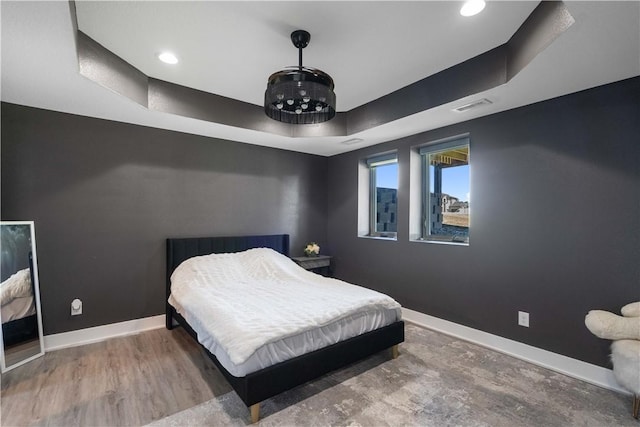 bedroom with wood finished floors, visible vents, baseboards, a tray ceiling, and recessed lighting