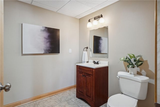 bathroom with toilet, vanity, tile patterned floors, and a paneled ceiling