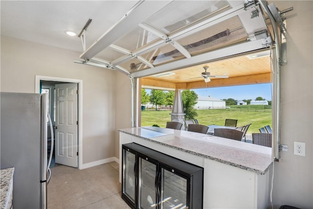 kitchen with white cabinetry, stainless steel refrigerator, ceiling fan, and light stone counters