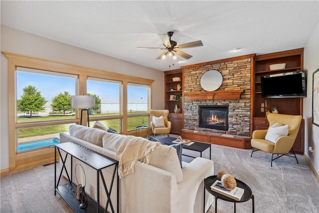 carpeted living room featuring built in shelves, ceiling fan, a stone fireplace, and a textured ceiling