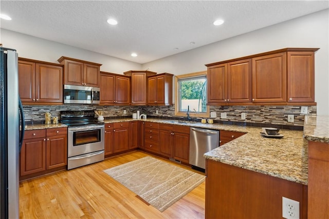 kitchen featuring light stone counters, sink, stainless steel appliances, and light wood-type flooring