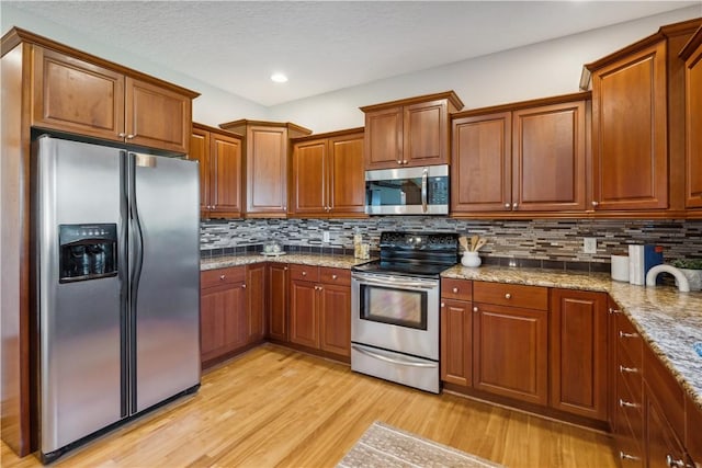 kitchen with light stone countertops, light wood-type flooring, stainless steel appliances, and backsplash