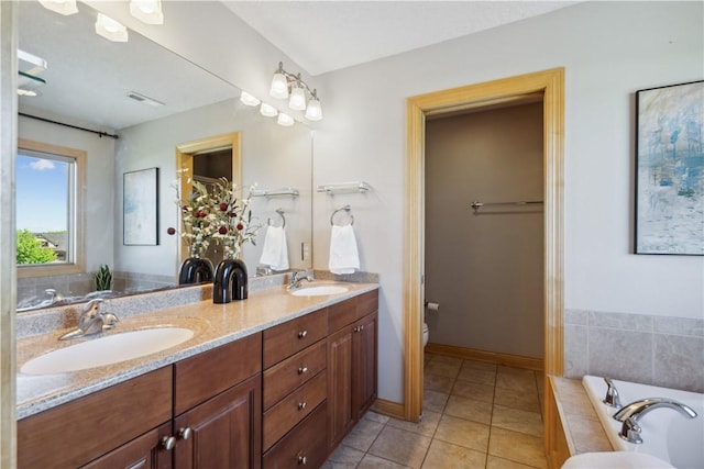 bathroom with tile patterned floors, vanity, a relaxing tiled tub, and toilet