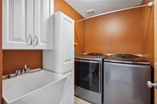 laundry room featuring a textured ceiling, washer and dryer, cabinets, and sink