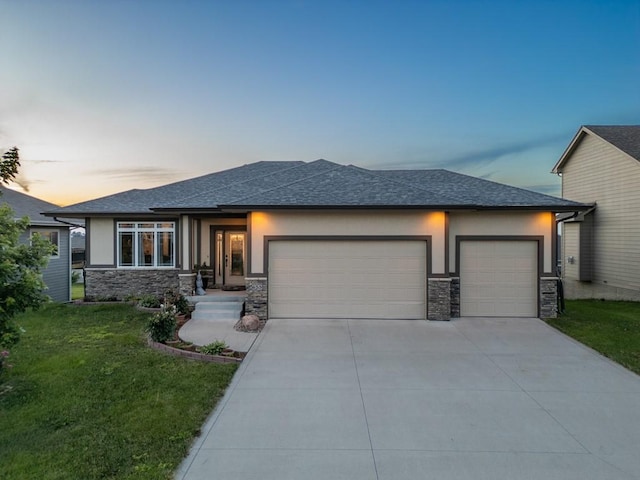 prairie-style house featuring stucco siding, driveway, a yard, stone siding, and an attached garage