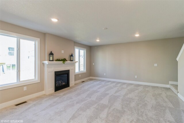 unfurnished living room with a textured ceiling, light colored carpet, and plenty of natural light