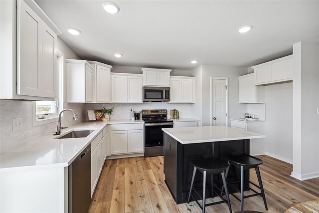 kitchen with white cabinets, light wood-type flooring, a kitchen island, a kitchen bar, and stainless steel appliances