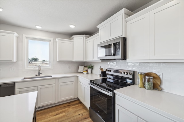 kitchen featuring light wood-type flooring, tasteful backsplash, stainless steel appliances, sink, and white cabinets