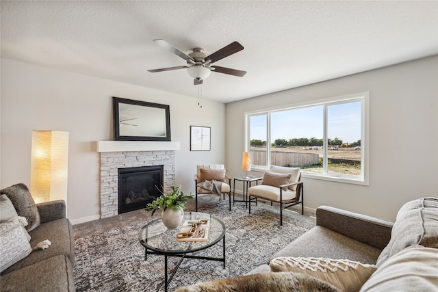 carpeted living room featuring a textured ceiling, a stone fireplace, and ceiling fan