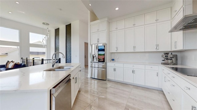 kitchen with stainless steel appliances, hanging light fixtures, white cabinetry, a sink, and wall chimney range hood