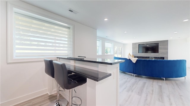 kitchen featuring visible vents, a kitchen breakfast bar, baseboards, light wood-style floors, and dark countertops