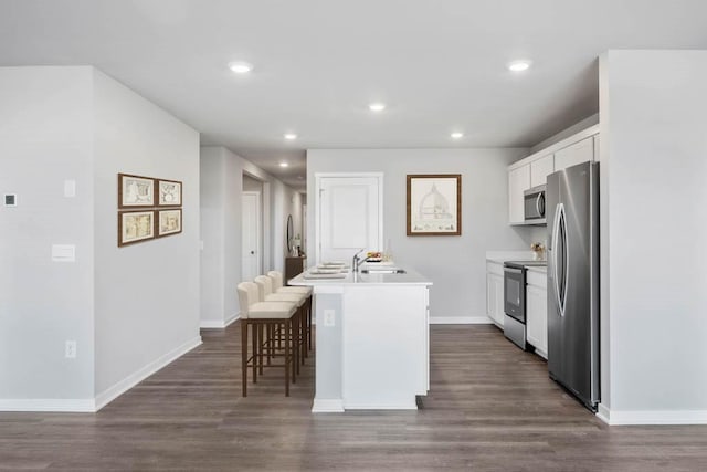 kitchen with a breakfast bar, an island with sink, appliances with stainless steel finishes, white cabinets, and dark wood-style flooring