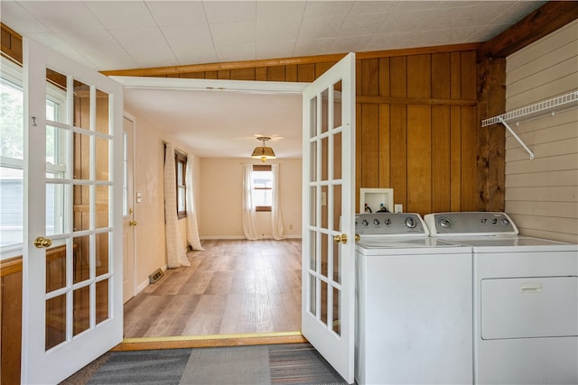 laundry room with wood walls, wood-type flooring, french doors, and separate washer and dryer