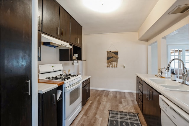 kitchen with white appliances, light hardwood / wood-style floors, dark brown cabinetry, and sink