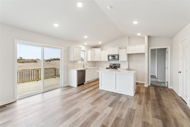 kitchen with light wood-type flooring, a center island, white cabinetry, stainless steel appliances, and vaulted ceiling