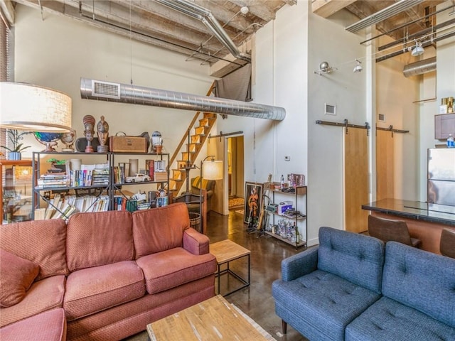 living area with concrete flooring, a barn door, a towering ceiling, visible vents, and stairway