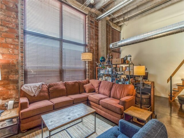 living room with brick wall, a high ceiling, and concrete flooring