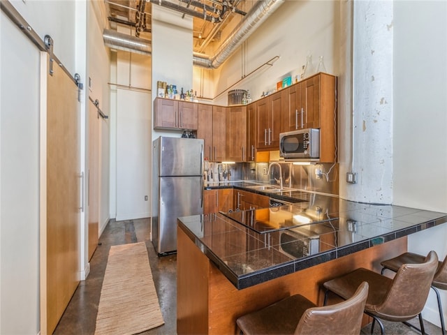 kitchen featuring a breakfast bar area, appliances with stainless steel finishes, a barn door, and tasteful backsplash