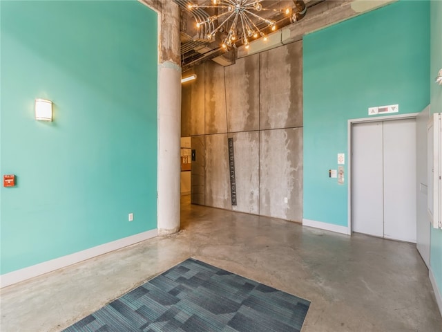 spare room featuring a chandelier, elevator, a towering ceiling, and concrete flooring