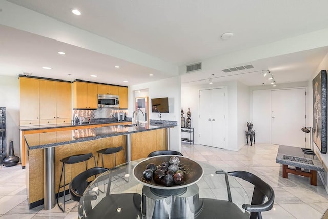 kitchen with sink, gas cooktop, tasteful backsplash, a large island with sink, and dark stone counters