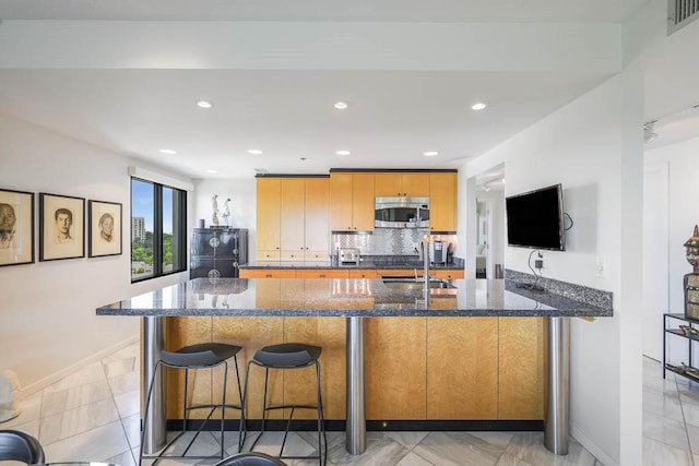 kitchen with decorative backsplash, a kitchen bar, black fridge, dark stone counters, and sink