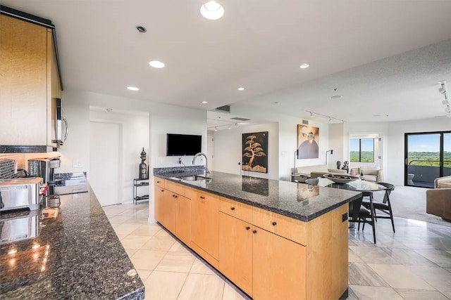 kitchen featuring light brown cabinetry, rail lighting, dark stone counters, sink, and a center island with sink