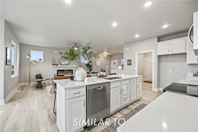 kitchen with stainless steel dishwasher, ceiling fan, sink, a center island with sink, and white cabinetry