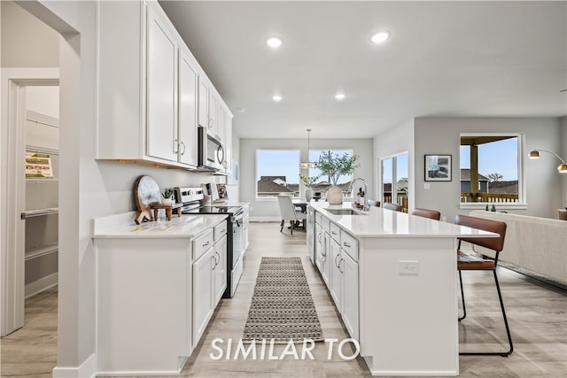 kitchen with appliances with stainless steel finishes, light wood-type flooring, a kitchen island with sink, and sink