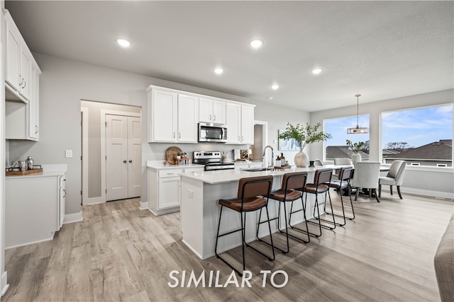 kitchen featuring stainless steel appliances, decorative light fixtures, light hardwood / wood-style flooring, white cabinets, and an island with sink