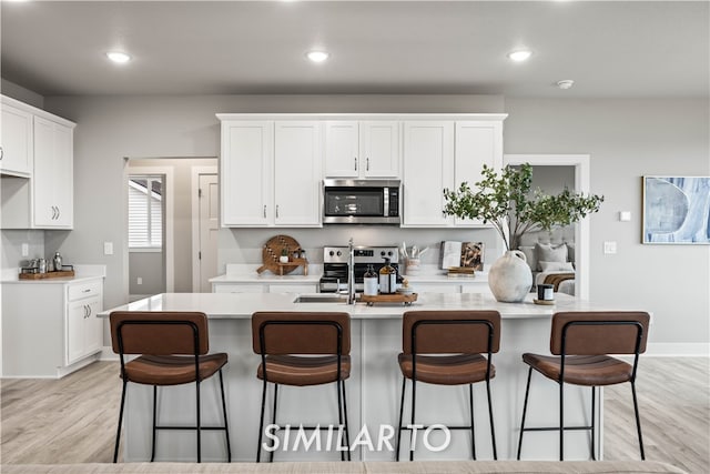 kitchen with a center island with sink, white cabinetry, light wood-type flooring, and stainless steel appliances