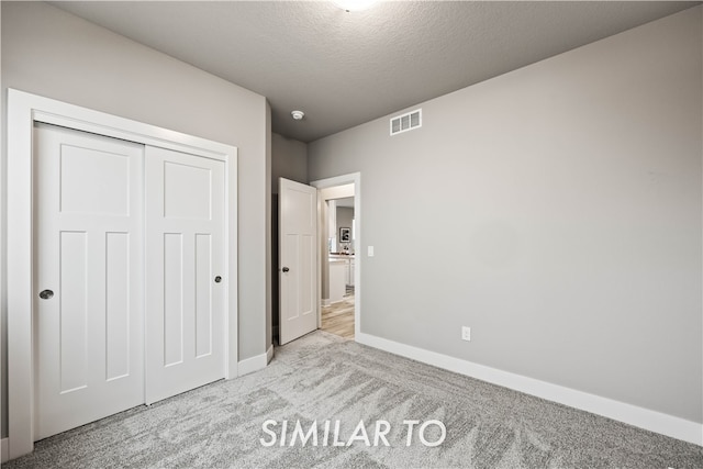 unfurnished bedroom with a closet, light colored carpet, and a textured ceiling