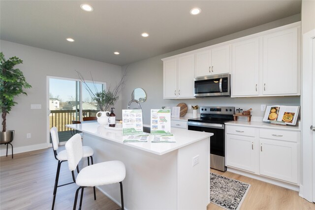 kitchen with white cabinets, a kitchen island with sink, stainless steel appliances, and light countertops