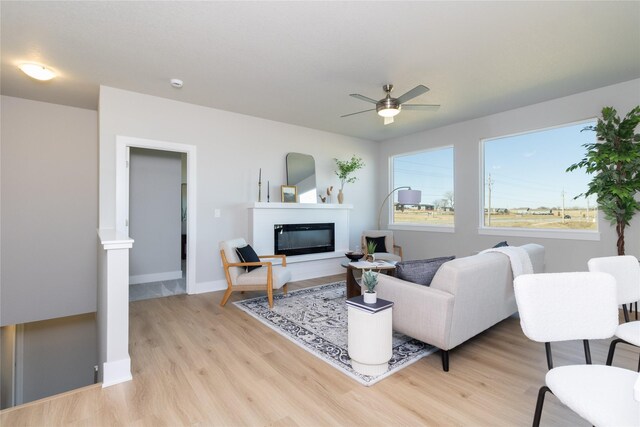 living room featuring light wood finished floors, baseboards, a ceiling fan, and a glass covered fireplace