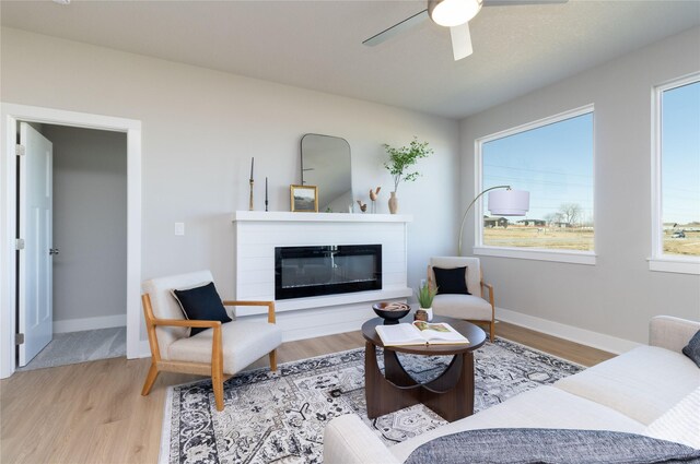 living room with light wood-style floors, a glass covered fireplace, ceiling fan, and baseboards