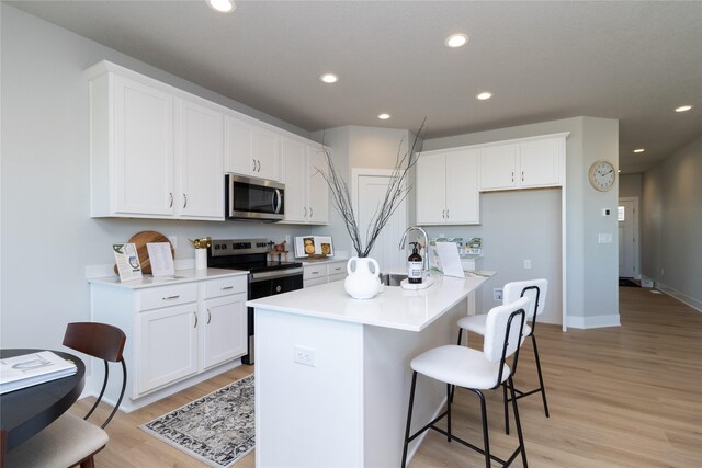 kitchen featuring white cabinets, a center island with sink, stainless steel appliances, and light countertops