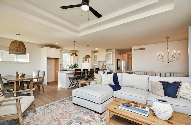 living room featuring ceiling fan with notable chandelier, sink, light hardwood / wood-style flooring, and a raised ceiling