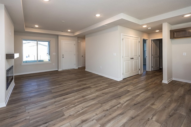 unfurnished living room with dark wood-type flooring and a tray ceiling