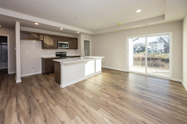 kitchen with a kitchen island with sink, sink, light hardwood / wood-style flooring, dark brown cabinetry, and stainless steel appliances