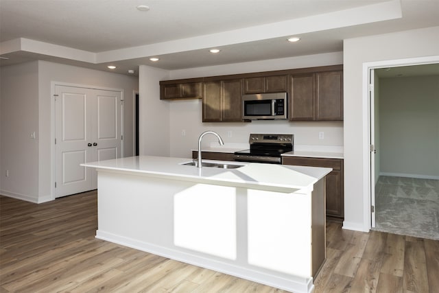 kitchen with dark brown cabinetry, sink, an island with sink, appliances with stainless steel finishes, and light wood-type flooring