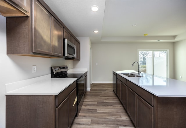 kitchen with dark brown cabinetry, sink, a kitchen island with sink, appliances with stainless steel finishes, and light wood-type flooring