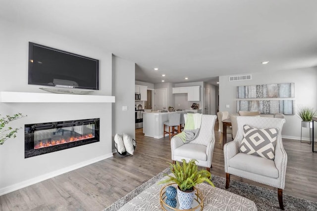 living area with visible vents, wood finished floors, a glass covered fireplace, recessed lighting, and baseboards