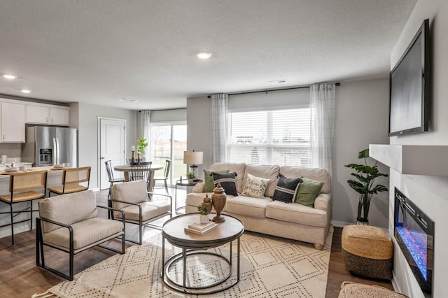 living room featuring wood finished floors, a textured ceiling, and a glass covered fireplace