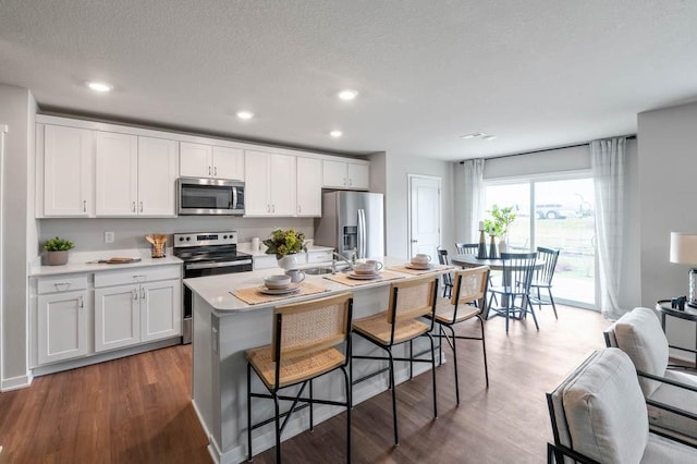 kitchen with white cabinetry, dark wood-type flooring, a textured ceiling, a center island with sink, and appliances with stainless steel finishes