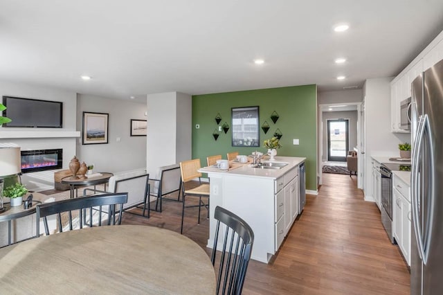 kitchen featuring an island with sink, stainless steel appliances, light countertops, white cabinets, and a glass covered fireplace