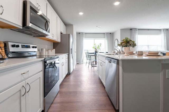 kitchen with white cabinets, a center island with sink, appliances with stainless steel finishes, and a sink